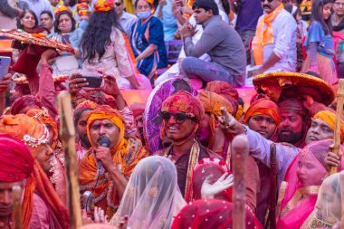 Barsana, Uttar Pradesh, India - March 18, 2024: Group of hindu male from nandgaon in traditional clothes and colorful faces celebrating the lathmar holi in rangili gali of barsana with tradition. clipart