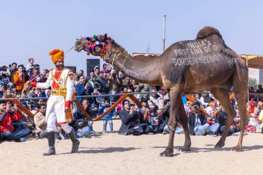 Bikaner, Rajasthan, Hindistan - 14 Ocak 2023: Deve festivali sırasında bikaner 'in kum tepelerinde bir rajasthani erkeğiyle yürüyen deve madalyası. Deve dansı en önemli eğlencedir..
