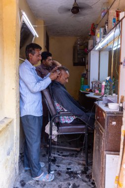 Naina Devi, Himachal Pradesh, Hindistan - 20 Mart 22: Erkek berber dükkanında müşterisine saçını kesiyor.