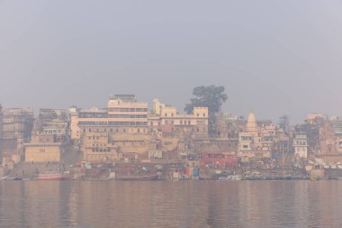 Varanasi, Uttar Pradesh, Hindistan - 20 Ocak 2024: Turistler sabahın erken saatlerinde Varanasi 'deki nehir çetelerinde tekne turunun keyfini çıkarıyorlar. Kayıkçı kışın sisli sabahında tahta teknede yelken açıyor..