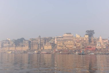 Varanasi, Uttar Pradesh, Hindistan - 20 Ocak 2024: Turistler sabahın erken saatlerinde Varanasi 'deki nehir çetelerinde tekne turunun keyfini çıkarıyorlar. Kayıkçı kışın sisli sabahında tahta teknede yelken açıyor..