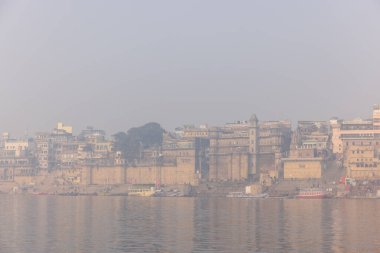 Varanasi, Uttar Pradesh, Hindistan - 20 Ocak 2024: Turistler sabahın erken saatlerinde Varanasi 'deki nehir çetelerinde tekne turunun keyfini çıkarıyorlar. Kayıkçı kışın sisli sabahında tahta teknede yelken açıyor..