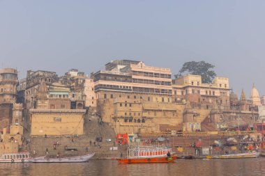 Varanasi, Uttar Pradesh, Hindistan - 20 Ocak 2024: Turistler sabahın erken saatlerinde Varanasi 'deki nehir çetelerinde tekne turunun keyfini çıkarıyorlar. Kayıkçı kışın sisli sabahında tahta teknede yelken açıyor..