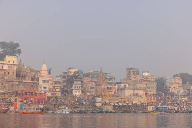 Varanasi, Uttar Pradesh, Hindistan - 20 Ocak 2024: Turistler sabahın erken saatlerinde Varanasi 'deki nehir çetelerinde tekne turunun keyfini çıkarıyorlar. Kayıkçı kışın sisli sabahında tahta teknede yelken açıyor..