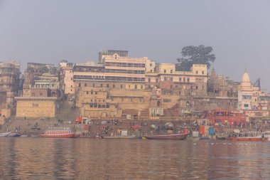 Varanasi, Uttar Pradesh, Hindistan - 20 Ocak 2024: Turistler sabahın erken saatlerinde Varanasi 'deki nehir çetelerinde tekne turunun keyfini çıkarıyorlar. Kayıkçı kışın sisli sabahında tahta teknede yelken açıyor..