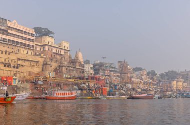Varanasi, Uttar Pradesh, Hindistan - 20 Ocak 2024: Turistler sabahın erken saatlerinde Varanasi 'deki nehir çetelerinde tekne turunun keyfini çıkarıyorlar. Kayıkçı kışın sisli sabahında tahta teknede yelken açıyor..