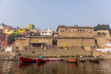 Varanasi, Uttar Pradesh, Hindistan - 20 Ocak 2024: Turistler sabahın erken saatlerinde Varanasi 'deki nehir çetelerinde tekne turunun keyfini çıkarıyorlar. Kayıkçı kışın sisli sabahında tahta teknede yelken açıyor..