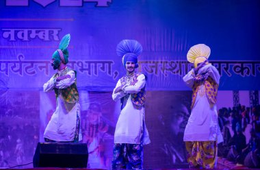 Pushkar, Rajasthan, Hindistan - 11 Kasım 2024: Bhangra, Sih erkek sanatçılar grubu renkli etnik elbiseler içinde bhangra dansı yapıyorlar..