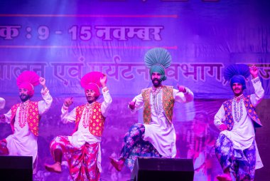 Pushkar, Rajasthan, Hindistan - 11 Kasım 2024: Bhangra, Sih erkek sanatçılar grubu renkli etnik elbiseler içinde bhangra dansı yapıyorlar..