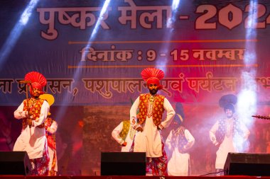Pushkar, Rajasthan, Hindistan - 11 Kasım 2024: Bhangra, Sih erkek sanatçılar grubu renkli etnik elbiseler içinde bhangra dansı yapıyorlar..