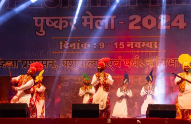 Pushkar, Rajasthan, Hindistan - 11 Kasım 2024: Bhangra, Sih erkek sanatçılar grubu renkli etnik elbiseler içinde bhangra dansı yapıyorlar..