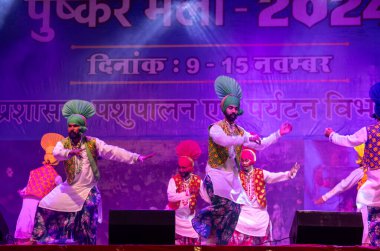 Pushkar, Rajasthan, Hindistan - 11 Kasım 2024: Bhangra, Sih erkek sanatçılar grubu renkli etnik elbiseler içinde bhangra dansı yapıyorlar..