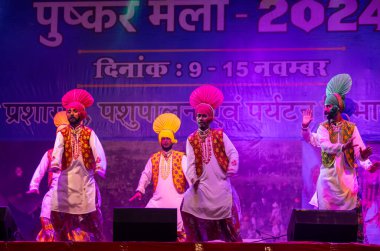 Pushkar, Rajasthan, Hindistan - 11 Kasım 2024: Bhangra, Sih erkek sanatçılar grubu renkli etnik elbiseler içinde bhangra dansı yapıyorlar..