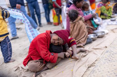 Prayagraj, Uttar Pradesh, Hindistan - 14 Ocak 2025: Mahakumbh, Paşagraj 'daki maha kumbh mela sırasında aileleriyle yol kenarında oturan bir grup çocuk.