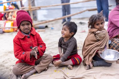 Prayagraj, Uttar Pradesh, Hindistan - 14 Ocak 2025: Mahakumbh, Paşagraj 'daki maha kumbh mela sırasında aileleriyle yol kenarında oturan bir grup çocuk.