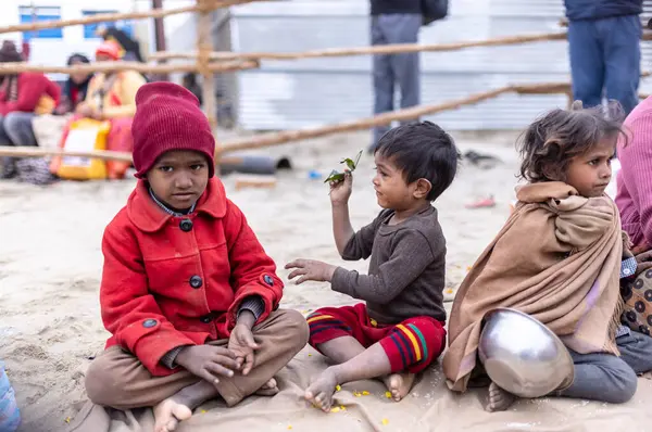Prayagraj, Uttar Pradesh, Hindistan - 14 Ocak 2025: Mahakumbh, Paşagraj 'daki maha kumbh mela sırasında aileleriyle yol kenarında oturan bir grup çocuk.