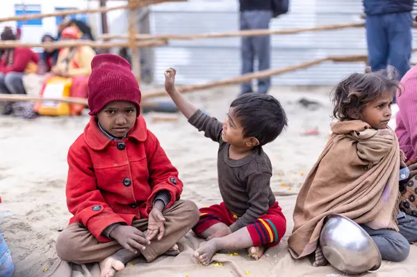 Prayagraj, Uttar Pradesh, Hindistan - 14 Ocak 2025: Mahakumbh, Paşagraj 'daki maha kumbh mela sırasında aileleriyle yol kenarında oturan bir grup çocuk.