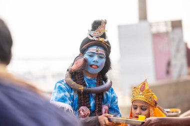 Varanasi, Uttar Pradesh, Hindistan - 20 Ocak 2024: Varanasi 'de kış sabahı Ganga nehrinde boyalı yüzüyle yürüyen Lord Shiv gibi giyinmiş genç bir çocuğun portresi.