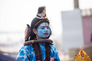 Varanasi, Uttar Pradesh, Hindistan - 20 Ocak 2024: Varanasi 'de kış sabahı Ganga nehrinde boyalı yüzüyle yürüyen Lord Shiv gibi giyinmiş genç bir çocuğun portresi.