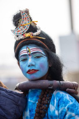 Varanasi, Uttar Pradesh, Hindistan - 20 Ocak 2024: Varanasi 'de kış sabahı Ganga nehrinde boyalı yüzüyle yürüyen Lord Shiv gibi giyinmiş genç bir çocuğun portresi.