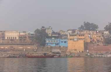 Varanasi, Uttar Pradesh, Hindistan - 20 Ocak 2024: Turistler sabahın erken saatlerinde Varanasi 'deki nehir çetelerinde tekne turunun keyfini çıkarıyorlar. Kayıkçı kışın sisli sabahında tahta teknede yelken açıyor..