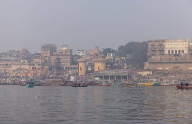 Varanasi, Uttar Pradesh, Hindistan - 20 Ocak 2024: Turistler sabahın erken saatlerinde Varanasi 'deki nehir çetelerinde tekne turunun keyfini çıkarıyorlar. Kayıkçı kışın sisli sabahında tahta teknede yelken açıyor..