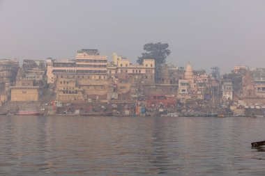Varanasi, Uttar Pradesh, Hindistan - 20 Ocak 2024: Turistler sabahın erken saatlerinde Varanasi 'deki nehir çetelerinde tekne turunun keyfini çıkarıyorlar. Kayıkçı kışın sisli sabahında tahta teknede yelken açıyor..