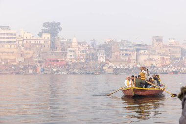Varanasi, Uttar Pradesh, Hindistan - 20 Ocak 2024: Turistler sabahın erken saatlerinde Varanasi 'deki nehir çetelerinde tekne turunun keyfini çıkarıyorlar. Kayıkçı kışın sisli sabahında tahta teknede yelken açıyor..