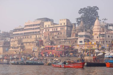 Varanasi, Uttar Pradesh, Hindistan - 20 Ocak 2024: Turistler sabahın erken saatlerinde Varanasi 'deki nehir çetelerinde tekne turunun keyfini çıkarıyorlar. Kayıkçı kışın sisli sabahında tahta teknede yelken açıyor..
