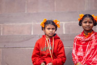 Varanasi, Uttar Pradesh, Hindistan - 20 Ocak 2024: Gurukul 'un veya okulun kimliği belirlenemeyen genç bayan öğrencileri kış sabahı Varanasi' de kutsal nehir keneviri yakınlarında basamaklarda oturuyorlar.
