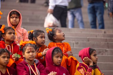 Varanasi, Uttar Pradesh, Hindistan - 20 Ocak 2024: Gurukul 'un veya okulun kimliği belirlenemeyen genç bayan öğrencileri kış sabahı Varanasi' de kutsal nehir keneviri yakınlarında basamaklarda oturuyorlar.