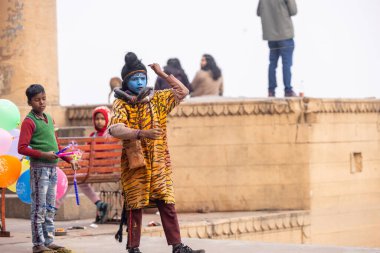 Varanasi, Uttar Pradesh, Hindistan - 20 Ocak 2024: Varanasi 'de kış akşamı kenevir nehrinde boyalı yüzlü uçan uçurtma gibi giyinmiş genç bir çocuğun portresi.