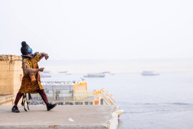 Varanasi, Uttar Pradesh, Hindistan - 20 Ocak 2024: Varanasi 'de kış sabahı Ganga nehrinde boyalı yüzüyle yürüyen Lord Shiv gibi giyinmiş genç bir çocuğun portresi.