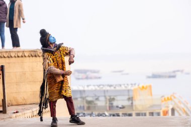 Varanasi, Uttar Pradesh, Hindistan - 20 Ocak 2024: Varanasi 'de kış sabahı Ganga nehrinde boyalı yüzüyle yürüyen Lord Shiv gibi giyinmiş genç bir çocuğun portresi.