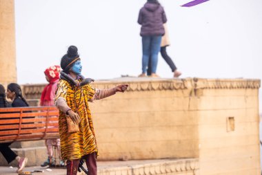 Varanasi, Uttar Pradesh, Hindistan - 20 Ocak 2024: Varanasi 'de kış sabahı Ganga nehrinde boyalı yüzüyle yürüyen Lord Shiv gibi giyinmiş genç bir çocuğun portresi.