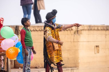 Varanasi, Uttar Pradesh, Hindistan - 20 Ocak 2024: Varanasi 'de kış sabahı Ganga nehrinde boyalı yüzüyle yürüyen Lord Shiv gibi giyinmiş genç bir çocuğun portresi.