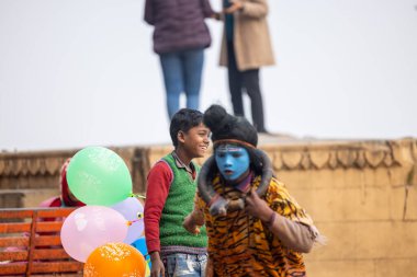 Varanasi, Uttar Pradesh, Hindistan - 20 Ocak 2024: Varanasi 'de kış sabahı Ganga nehrinde boyalı yüzüyle yürüyen Lord Shiv gibi giyinmiş genç bir çocuğun portresi.