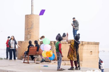 Varanasi, Uttar Pradesh, Hindistan - 20 Ocak 2024: Varanasi 'de kış sabahı Ganga nehrinde boyalı yüzüyle yürüyen Lord Shiv gibi giyinmiş genç bir çocuğun portresi.