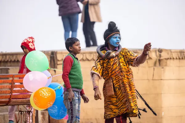 Varanasi, Uttar Pradesh, Hindistan - 20 Ocak 2024: Varanasi 'de kış sabahı Ganga nehrinde boyalı yüzüyle yürüyen Lord Shiv gibi giyinmiş genç bir çocuğun portresi.