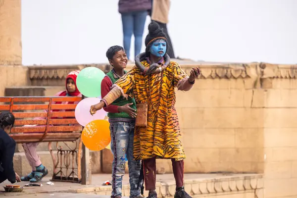 Varanasi, Uttar Pradesh, Hindistan - 20 Ocak 2024: Varanasi 'de kış sabahı Ganga nehrinde boyalı yüzüyle yürüyen Lord Shiv gibi giyinmiş genç bir çocuğun portresi.