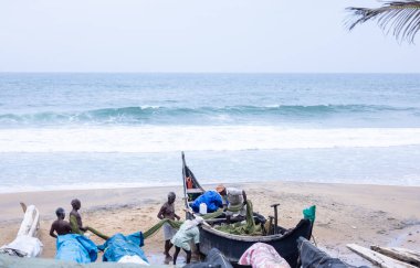 Thiruvananthapuram, Kerala, Hindistan - 14 Ekim 2024: Balıkları balık ağından çıkarmak için sahile park etmiş ahşap teknenin yanında duran yaşlı erkek balıkçılar grubu. İş yerinde tanıştık..