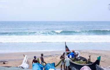 Thiruvananthapuram, Kerala, Hindistan - 14 Ekim 2024: Balıkları balık ağından çıkarmak için sahile park etmiş ahşap teknenin yanında duran yaşlı erkek balıkçılar grubu. İş yerinde tanıştık..