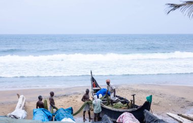 Thiruvananthapuram, Kerala, Hindistan - 14 Ekim 2024: Balıkları balık ağından çıkarmak için sahile park etmiş ahşap teknenin yanında duran yaşlı erkek balıkçılar grubu. İş yerinde tanıştık..