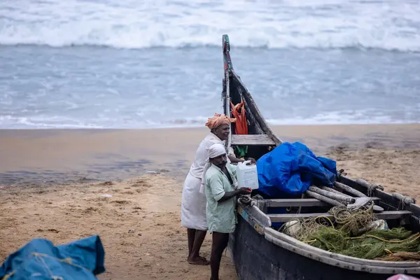 Thiruvananthapuram, Kerala, Hindistan - 14 Ekim 2024: Balıkları balık ağından çıkarmak için sahile park etmiş ahşap teknenin yanında duran yaşlı erkek balıkçılar grubu. İş yerinde tanıştık..