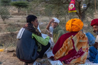 Puşkar, Rajasthan, Hindistan - Kasım 09 2024: Geleneksel beyaz giysili rajasthani erkek portresi çöl panayırında deve fuarı sırasında deve ticareti sırasında sarıklı.