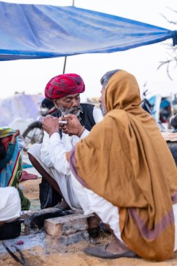 Puşkar, Rajasthan, Hindistan - Kasım 09 2024: Geleneksel beyaz giysili rajasthani erkek portresi çöl panayırında deve fuarı sırasında deve ticareti sırasında sarıklı.