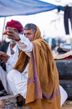Puşkar, Rajasthan, Hindistan - Kasım 09 2024: Geleneksel beyaz giysili rajasthani erkek portresi çöl panayırında deve fuarı sırasında deve ticareti sırasında sarıklı.