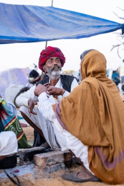 Puşkar, Rajasthan, Hindistan - Kasım 09 2024: Geleneksel beyaz giysili rajasthani erkek portresi çöl panayırında deve fuarı sırasında deve ticareti sırasında sarıklı.