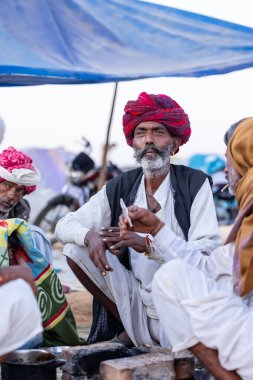 Puşkar, Rajasthan, Hindistan - Kasım 09 2024: Geleneksel beyaz giysili rajasthani erkek portresi çöl panayırında deve fuarı sırasında deve ticareti sırasında sarıklı.