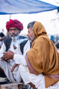 Puşkar, Rajasthan, Hindistan - Kasım 09 2024: Geleneksel beyaz giysili rajasthani erkek portresi çöl panayırında deve fuarı sırasında deve ticareti sırasında sarıklı.